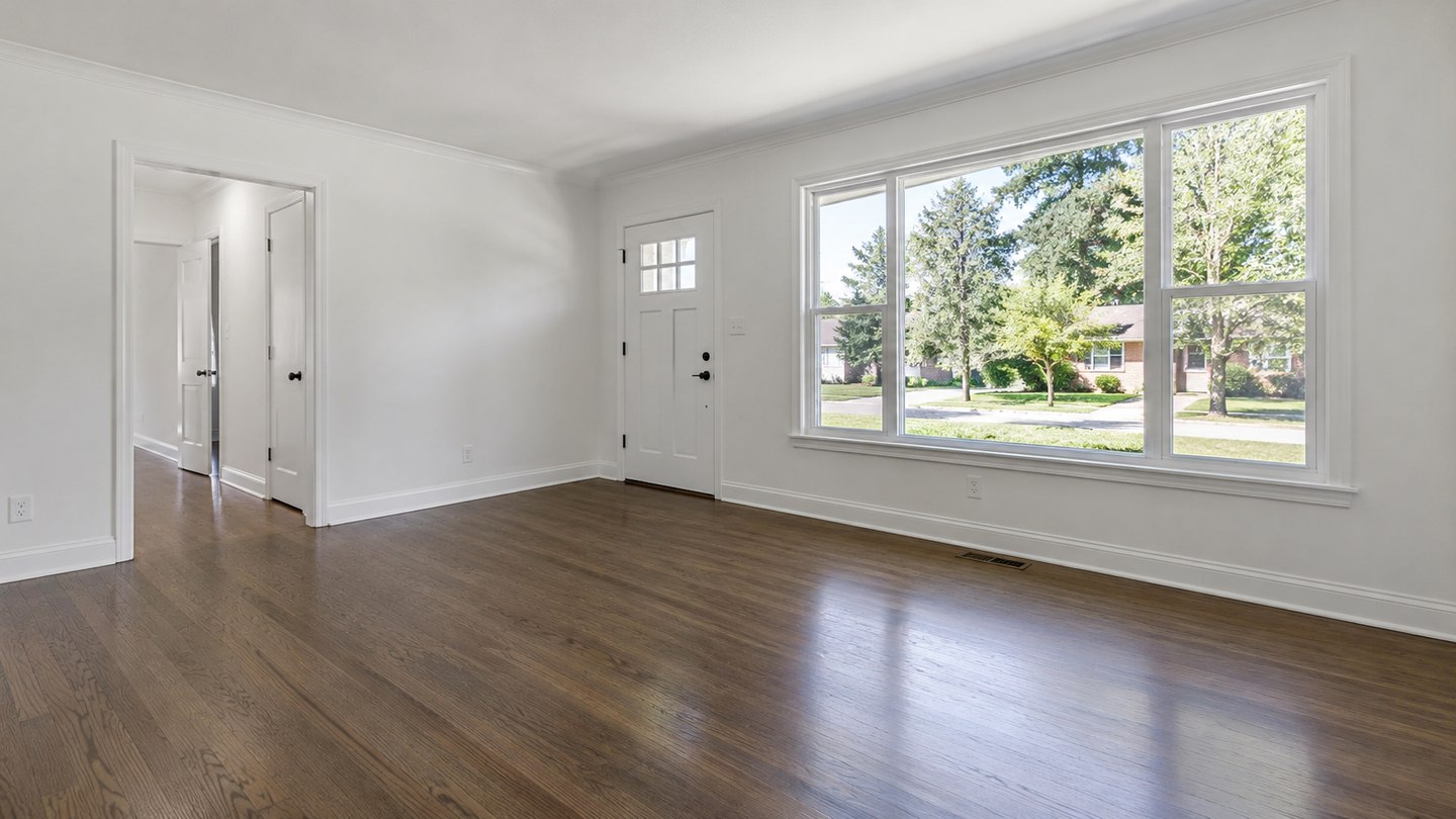 Empty clean residential room with white baseboards, wood floor and a broad front window
